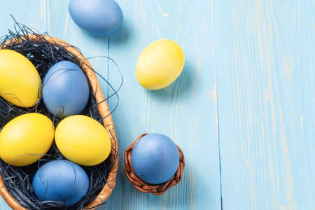 Easter composition - several colored eggs in a basket on a blue wooden table, place for text, copy spaceの写真素材