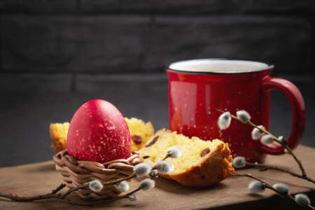 Red Easter egg, a slice of Easter cake and a cup of coffee on a cutting board on a dark table -...
