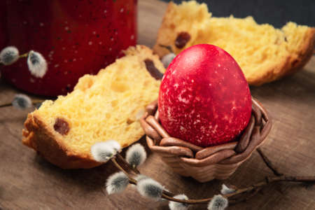 Red Easter egg, a slice of Easter cake and a cup of coffee on a cutting board on a dark table -...