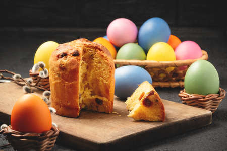 Easter cake on a cutting board and colored eggs on a table and in a wicker basket - traditional...