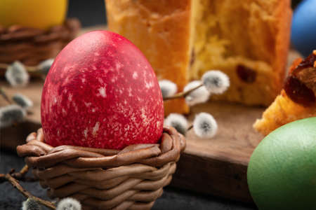Red Egg in a wicker stand, Easter cake on a cutting board and painted eggs on the table -...
