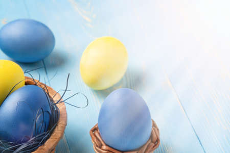 Easter composition - several colored eggs in a basket on a blue wooden table, place for text, copy...
