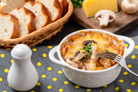 Casserole with chicken, mushrooms and cheese, known in Russia as julienne in white bowl with herbs on a kitchen towelの写真素材