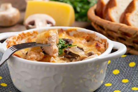 Casserole with chicken, mushrooms and cheese, known in Russia as julienne in white bowl with herbs on a kitchen towel, close upの写真素材