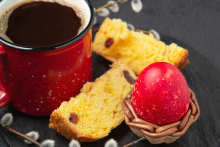 Red Easter egg, a slices of Easter cake and a cup of coffee on a cutting board on a dark table - traditional Easter breakfastの写真素材