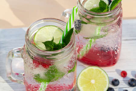 Homemade cold summer cocktail with mineral water, mint, lime, berry juice and fresh berries.
