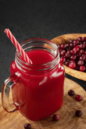 Healing cranberry juice in a glass jar-mug with a straw on black table. Healthy eating concept, vertical image.の写真素材