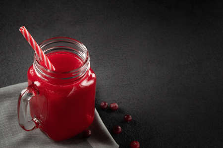 Healing cranberry juice in a glass jar-mug with a straw on black table. Healthy eating concept with...