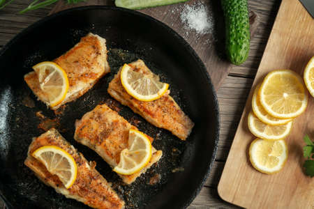 Portioned pieces of fried fish in a black cast-iron pan with fresh cucumbers and herbs. Traditional...