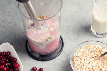 Making homemade smoothie with yoguot, cranberries and oatmeal. Beating a blender for healthy and...