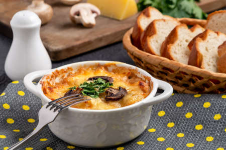 Casserole with chicken, mushrooms and cheese, known in Russia as julienne in white bowl with herbs on a kitchen towelの写真素材