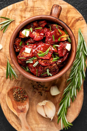 Sun-dried tomatoes with garlic, rosemary and spices in a clay bowl on an olive wood cutting board, top view, flat lay, vertical imageの写真素材