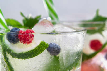 Homemade cold summer cocktail with mineral water, ice cubes, mint, lime, berry juice and fresh...