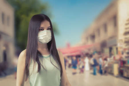 Young woman tourist in a protective medical mask on a street of a southern city. Coronavirus COVID-19 prevention measures conceptの写真素材
