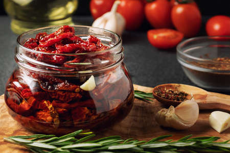 Sun-dried tomatoes with garlic, rosemary and spices in a glass jar on an olive wood cutting board.の写真素材