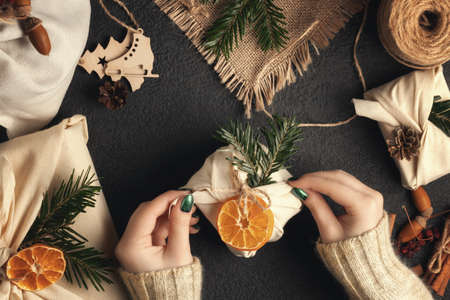Zero waste and eco friendly christmas concept. Female hands wrap gifts in natural fabric with ornaments made of natural materials, top view, flat layの写真素材