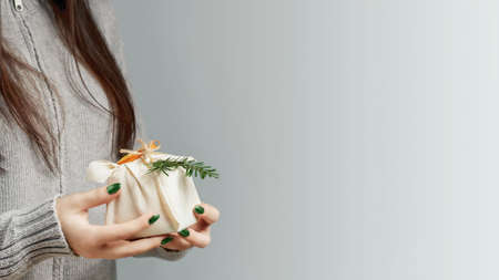 Zero waste and eco friendly christmas concept. Young woman holding in her hands a gift wrapped in natural fabric and decorated with natural materialsの写真素材
