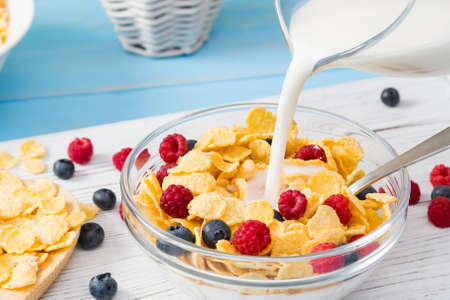 Pouring milk into a cup with cereal and fresh berries, close-up. Healthy summer breakfast. Healthy eating conceptの写真素材