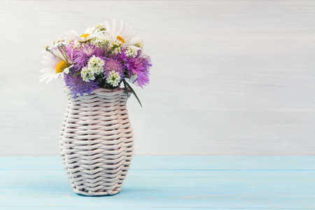 Delicate cute wildflowers in a light wicker vase on a blue wooden table, copy space for textの写真素材