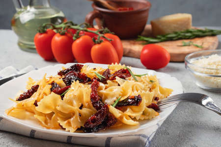Pasta with sun-dried tomatoes and parmesan in a white plate on the table. Italian cuisine, ingredients and the finished dishの写真素材