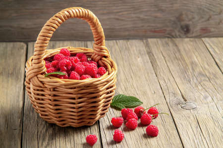 Ripe forest raspberries in a small basket on a wooden table, copy space.