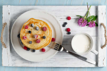 Stack of pancakes with fresh berries on a white plate a cup of milk and wildflowers on the table, top viewの写真素材