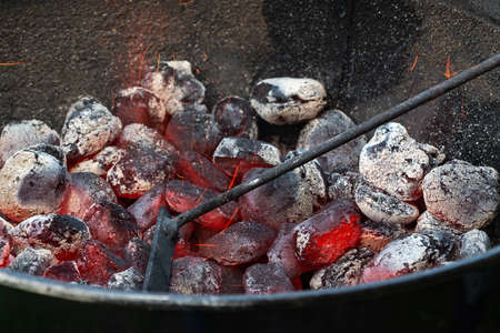 Stirring with a poker hot charcoal in a round barbecue grillの写真素材