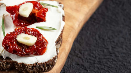 Homemade multigrain bread sandwiches with cream cheese and sun-dried tomatoes on a wooden platter. Healthy eating concept, copy spaceの写真素材
