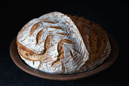 Homemade round dark bread with flour crust and painted spikelet on a clay plate