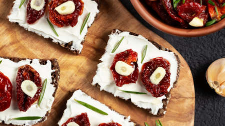 Homemade multigrain bread sandwiches with cream cheese and sun-dried tomatoes on a wooden platter. Healthy eating concept. Flat lay, topviewの写真素材