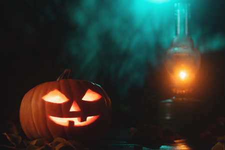 Halloween pumpkin head jack lantern with glowing eyes and kerosene lamp on wooden tableの写真素材