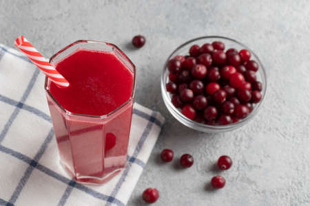 One glass with homemade freshly cranberry juice and a bowl of cranberries on a gray concrete tableの写真素材