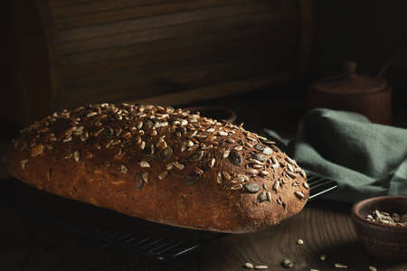Loaf of homemade whole grain bread with seeds cool down on a wire rack on a wooden table