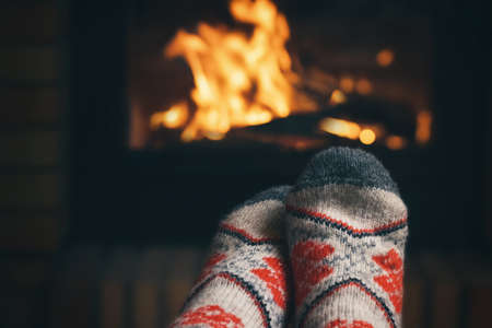 Girl resting and warming her feet by a burning fireplace in a country house on a winter evening. Selective focus.の写真素材
