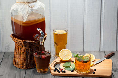 Homemade mushroom kombucha drink in a jar with a tap and in glasses with mint, berries and lemon on a wooden tableの写真素材