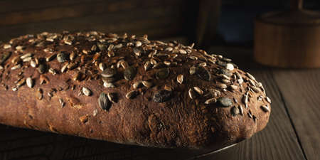 Loaf of homemade whole grain bread with seeds cool down on a wire rack on a wooden table