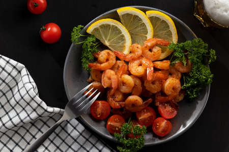 Served dinner - fried shrimp with lemon, tomatoes and herbs and beer in a glass on the table, top view, flat layの写真素材