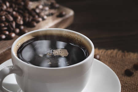 White cup of fresh hot coffee and coffee beans on wooden board on table, close upの写真素材