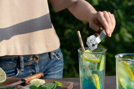 Girl makes summer refreshing cocktails lagoon. Close-up of adding ice cubes to glasses. Selective focusの写真素材