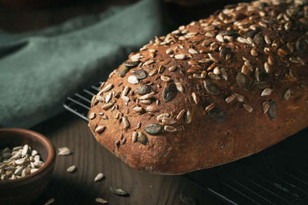 Loaf of homemade whole grain bread with seeds cool down on a wire rack on a wooden tableの写真素材