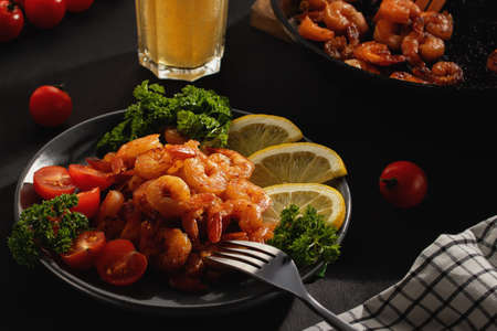Served dinner - fried shrimp with lemon, tomatoes and herbs and beer in a glass on the tableの写真素材