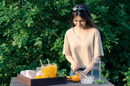 Girl cooking summer orange cocktail with mint and ice cubes outdoors, selective focusの写真素材