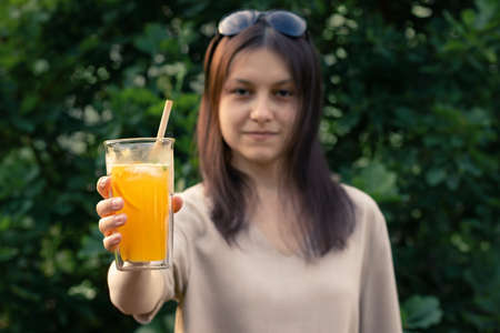Beautiful girl holds out a glass with a fresh orange summer cocktail, selective focusの写真素材