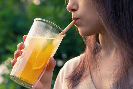 Girl drinks from a glass with fresh orange summer cocktail, close-up, selective focusの写真素材