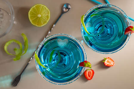 Fresh homemade blue margarita cocktail garnished with lime zest and strawberriesの写真素材