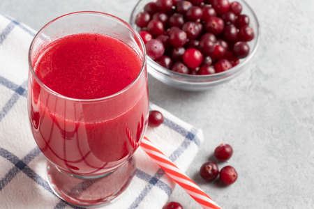 One glass with homemade freshly cranberry juice and a bowl of cranberries on a gray concrete tableの写真素材