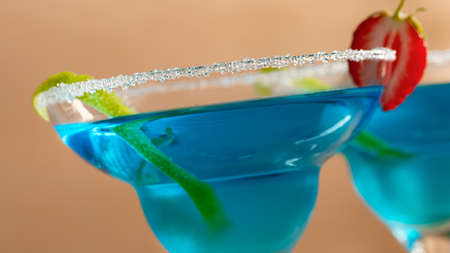 Two glasses with blue margarita cocktail garnished with lime zest and strawberries, selective focusの写真素材