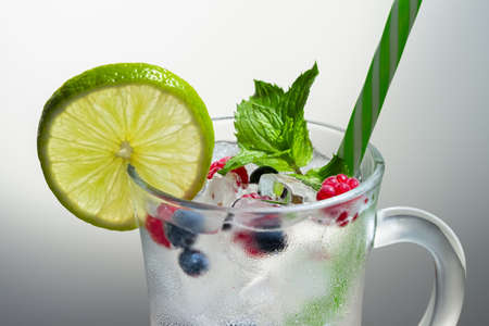 Refreshing summer cocktail with ice, lime and berries in a glass with a strawの写真素材