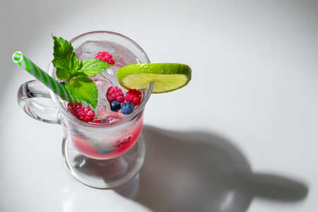 Refreshing summer cocktail with ice, lime and berries in a glass with a straw, copyspaceの写真素材