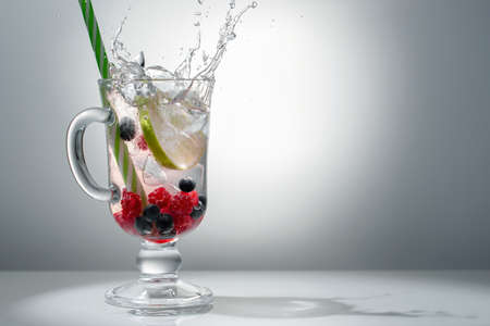 Refreshing summer cocktail with ice, lime and berries in a glass with a straw, copyspaceの写真素材